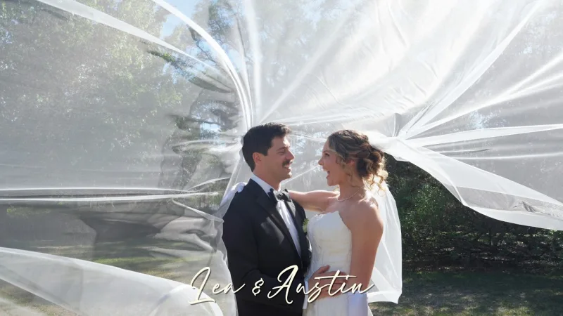 A bride and groom laughing face to face outdoors under tall trees as her long veil billows in the wind around them, with the names Lea and Austin written in script across the bottom