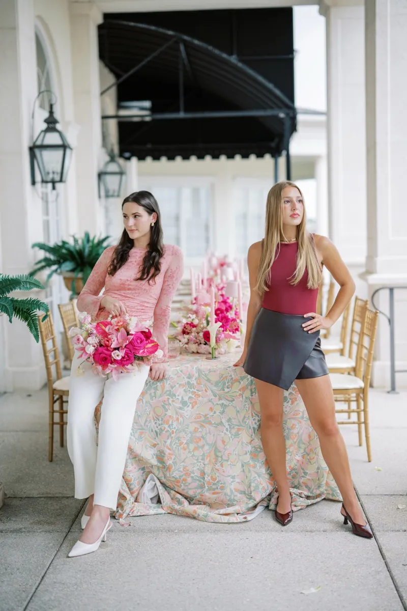 The Blue Tulip owner Madelyn Price, holding a hot pink bouquet, and floral designer Caroline Etter beside a long table of pink florals and taper candles on a marbled tablecloth